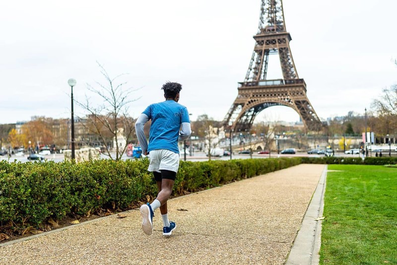 Young man exercising outdoors on a gravel path in paris, enjoying a fitness run with the iconic eiffel tower in the background, promoting active urban lifestyle and tourism