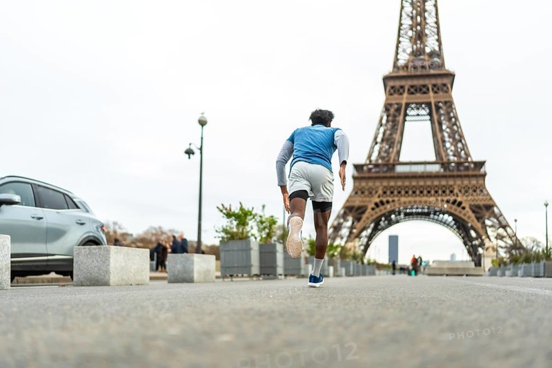 Athletic man sprinting through paris streets for urban training and fitness, eiffel tower rising behind him as he pushes for health, energy and focused performance