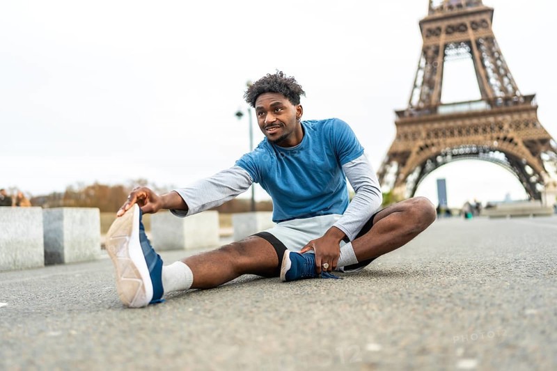 Young black man stretching on the ground, preparing for exercise with the iconic eiffel tower in the background, promoting fitness and an active lifestyle in an urban environment