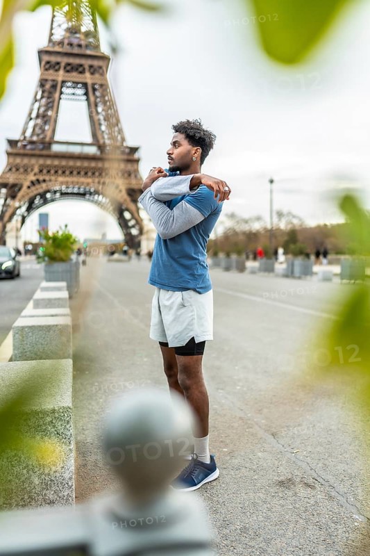 Young athletic man stretching his arms and shoulders on a city street in paris, preparing for an urban run with the iconic eiffel tower visible in the background