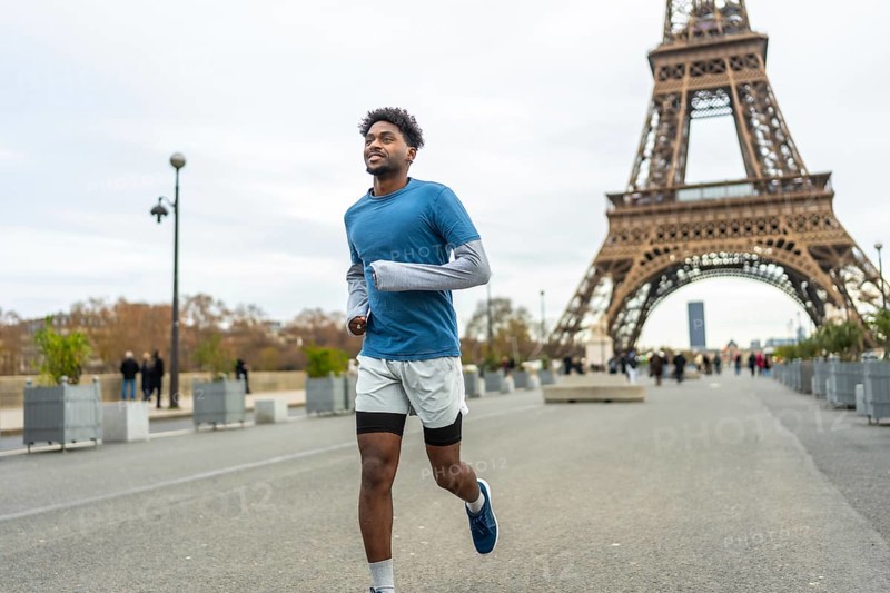 Young adult man with an arm prosthesis is running and smiling along the seine river with the iconic eiffel tower in the background, enjoying his fitness activity outdoors