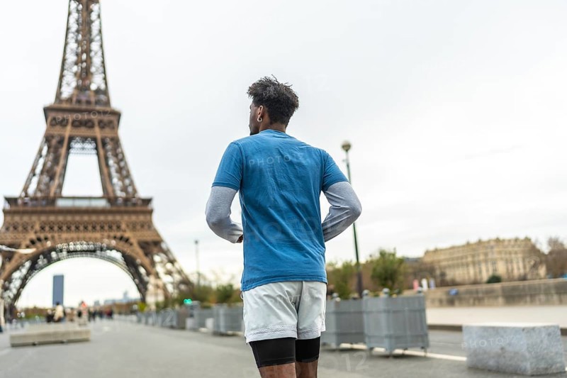 Adult man with dark skin running and training in the city of paris with the famous eiffel tower in the background on an overcast day, enjoying outdoor sport