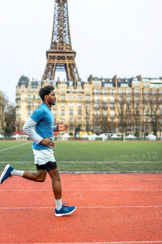 Young man running on an outdoor track in paris, training for fitness and endurance with the eiffel tower and urban cityscape framing his focused, energetic workout