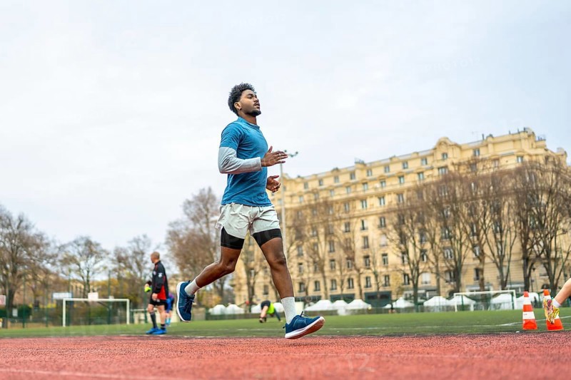 Young man training on a paris stadium running track, jogging in sportswear with focused determination, showcasing urban fitness, endurance and active healthy lifestyle outdoors