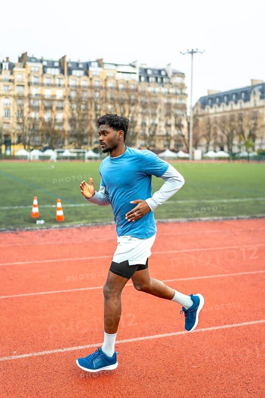 Young dark skinned athlete sprinting on a red urban track in paris, full body side view capturing motion, endurance and fitness in daytime city sports field with architecture backdrop