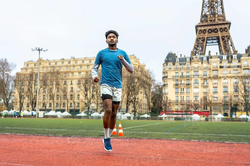 Young athletic man running on an outdoor track in paris, focusing on urban sport performance and fitness training with a famous landmark in the background