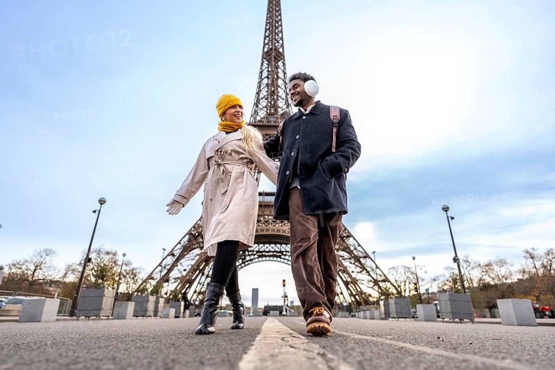 Diverse couple walking outdoors in paris holding hands, enjoying a romantic trip together on a winter day with the iconic eiffel tower in the background