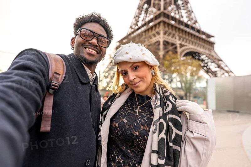Diverse couple smiling for a close up selfie in front of the eiffel tower, embracing travel and romance on a stylish paris city break, enjoying winter coats and scarves