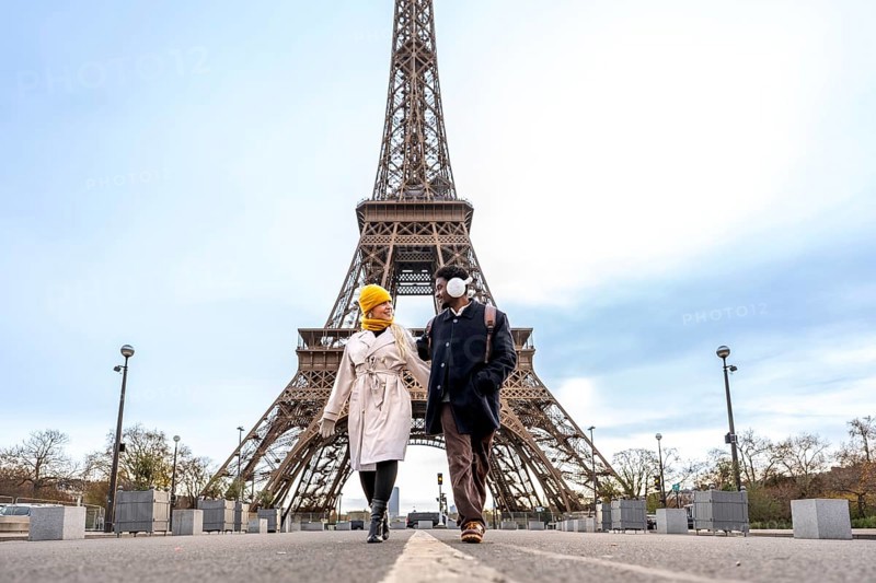 Young diverse couple walking and smiling together in front of the eiffel tower, embracing romance, tourism, and travel in the iconic city of paris, france