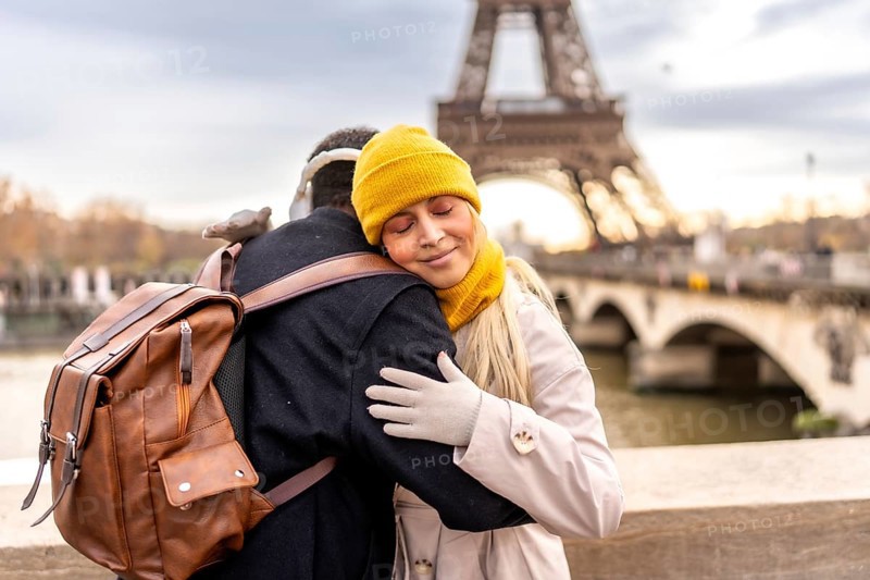 Young diverse couple embraces on a paris bridge, sharing a tender moment with the eiffel tower and seine softly blurred in the winter cityscape background