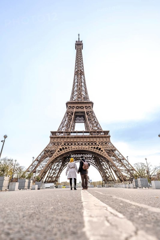 Couple holding hands walking down a street with a white line towards the eiffel tower on a bright day in paris, france, representing travel, romance, and shared experiences in a famous european city