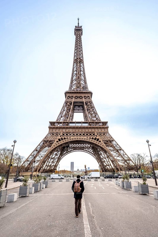 Solo traveler with backpack walks down a paris street toward the iconic eiffel tower, contemplating the historic iron landmark and cityscape during a solitary urban sightseeing moment