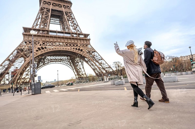 Happy couple holding hands and pointing toward the iconic eiffel tower while walking paris streets on a romantic sightseeing trip through europe, enjoying travel and discovery