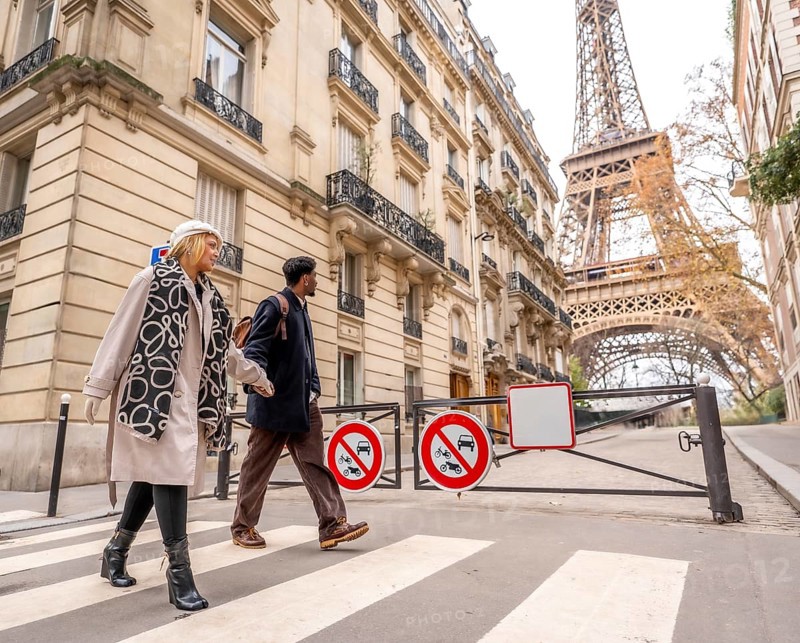 Diverse couple crossing a pedestrian street in paris, enjoying a city trip together with classical architecture and the iconic eiffel tower in the background