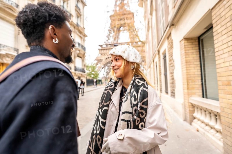 Happy diverse couple smiling and interacting on a parisian street with the eiffel tower in the background, symbolizing romance, travel, and urban exploration