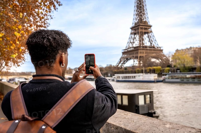 Traveler capturing a moment on smartphone while visiting the iconic eiffel tower in paris, engaging with city landmarks and culture during a european autumn trip