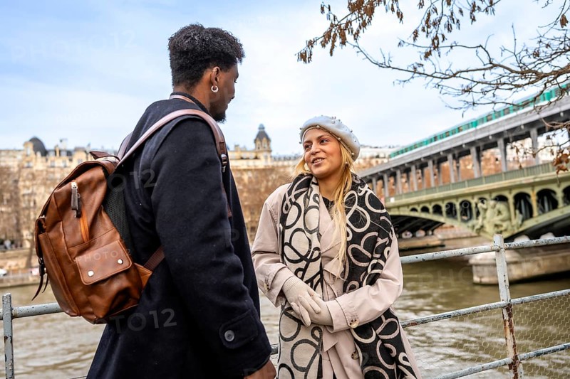Diverse young couple chatting on bir hakeim bridge over the seine in paris, sharing a romantic winter city moment while sightseeing, walking and connecting by the riverbank