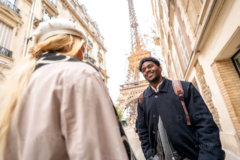 Happy young african american man smiling at his partner while enjoying a romantic trip in paris, with the eiffel tower and cityscape in the blurred background