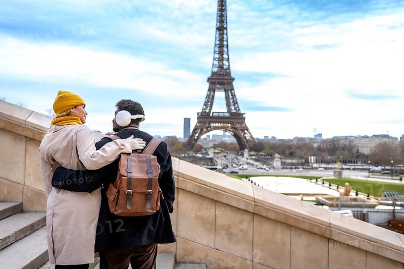 Young couple embracing on outdoor stairs with the eiffel tower in view, sharing a romantic winter moment in paris during a cozy sightseeing getaway