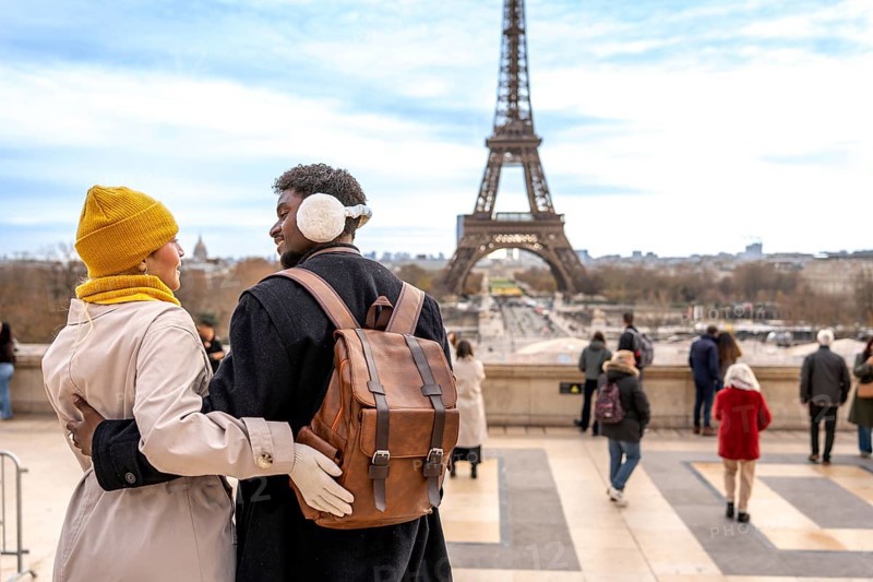 Young diverse couple embracing, traveling to paris, france, enjoying a romantic trip, sightseeing at trocadero with the eiffel tower in the background on a cold day