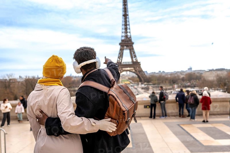 Young couple embracing and looking at the eiffel tower, the man pointing towards the landmark while enjoying a romantic winter travel experience in paris