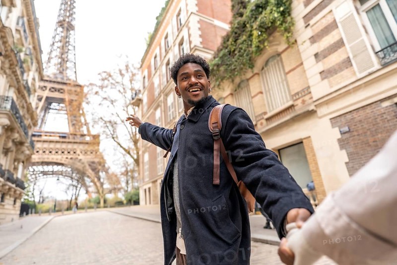Happy young man of african descent leads his partner by the hand, pointing toward the eiffel tower while smiling during a romantic city break in paris, france