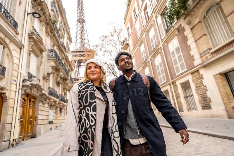 Diverse couple exploring a street in paris, france, looking up at the eiffel tower, experiencing romance and cultural tourism during their european vacation