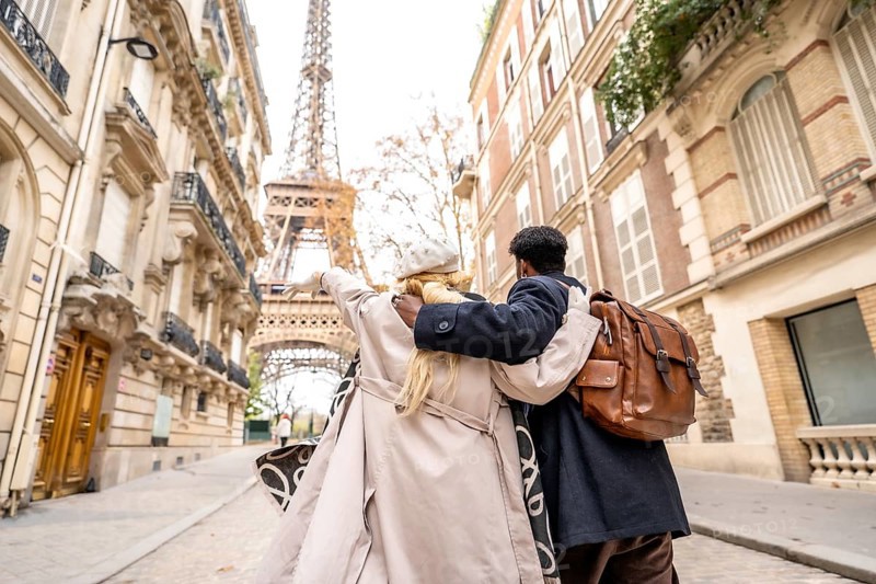 Happy traveling couple embracing as they walk down a cobblestone paris street, pointing toward the eiffel tower and discovering the city on a romantic sightseeing getaway