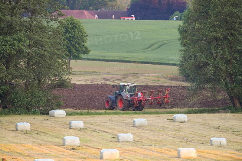 A tractor working in the field, surrounded by green fields and round bales of hay bales in a rural area, Osnabrücker Land, Lower Saxony, Germany