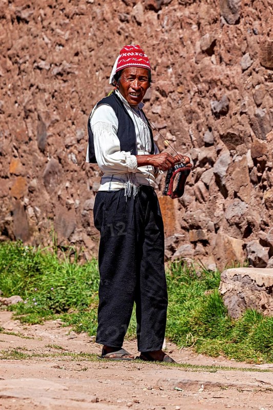 Man wearing a red cap and traditional clothing walks along a stone wall, The knitting men on Taquile Island in Lake Titicaca in Peru
