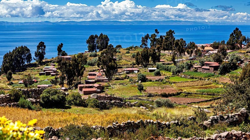 Small huts and fields on terraces overlooking a large lake, countryside and farmhouses on Taquile Island in Lake Titicaca in Peru