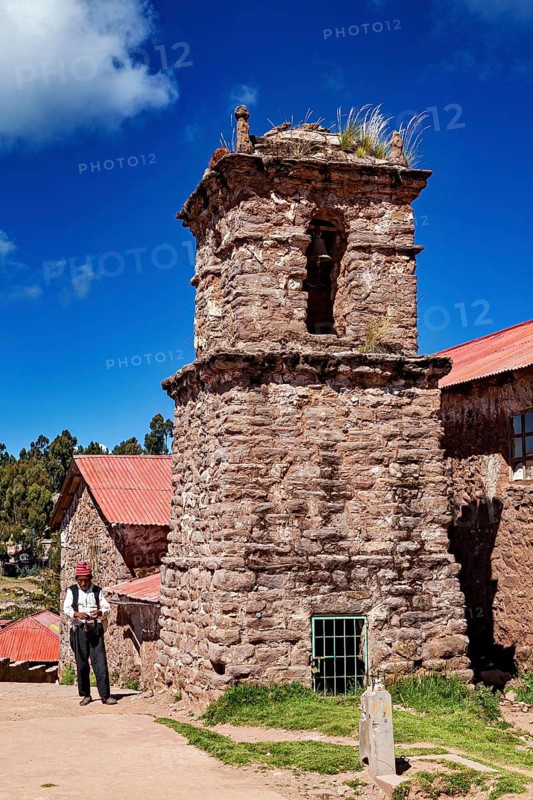 Old church tower with stone tower and a man in traditional clothing, The knitting men on the island of Taquile in Lake Titicaca in Peru