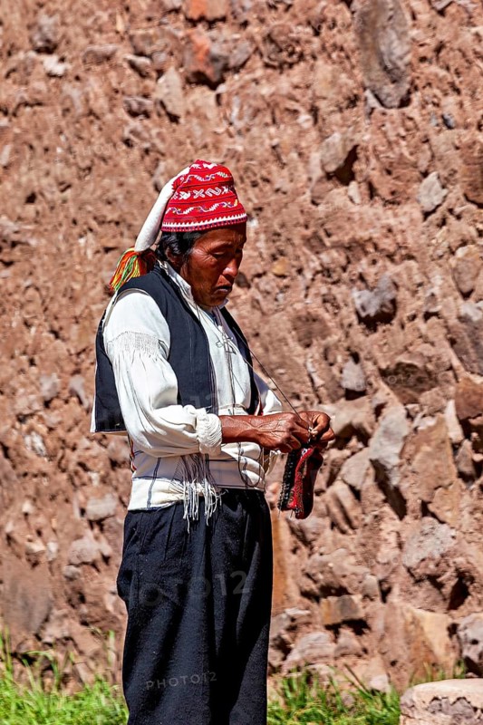 Close-up of a man wearing a red cap and traditional clothes on a stone wall, The knitting men on the island of Taquile in Lake Titicaca in Peru