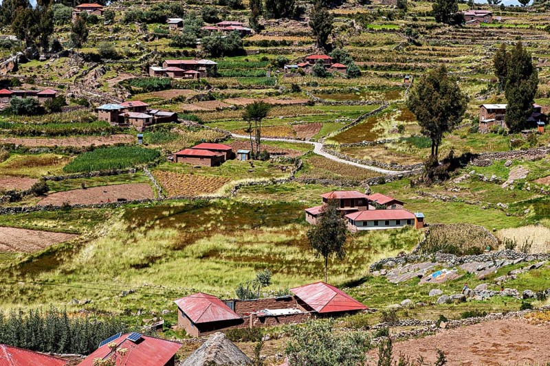 Small village with red roof huts on terraces surrounded by green fields, countryside and farmhouses on the island of Taquile in Lake Titicaca in Peru