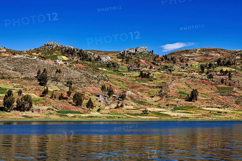 Wide fields stretch across rolling hills overlooking a lake, countryside and farmhouses on Taquile Island in Lake Titicaca in Peru