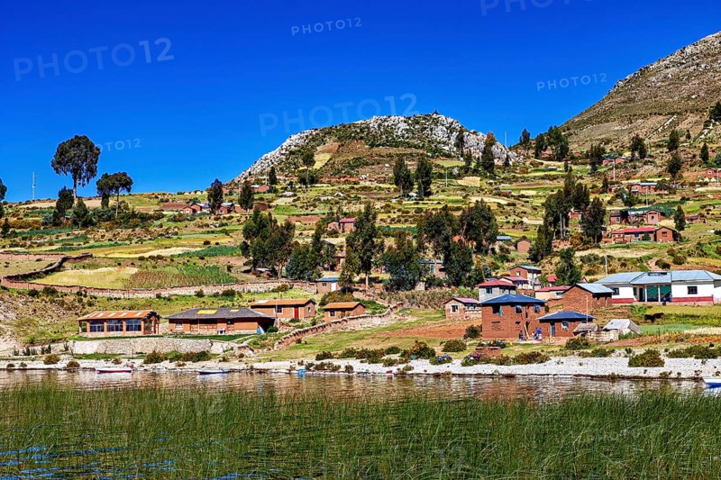 Idyllic village with lakeside farm houses and fields under blue skies, the countryside and farmhouses on Taquile Island in Lake Titicaca in Peru