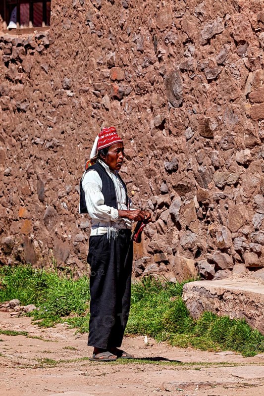 Elderly man wearing traditional clothes next to a stone wall under clear skies, The knitting men on Taquile Island in Lake Titicaca in Peru