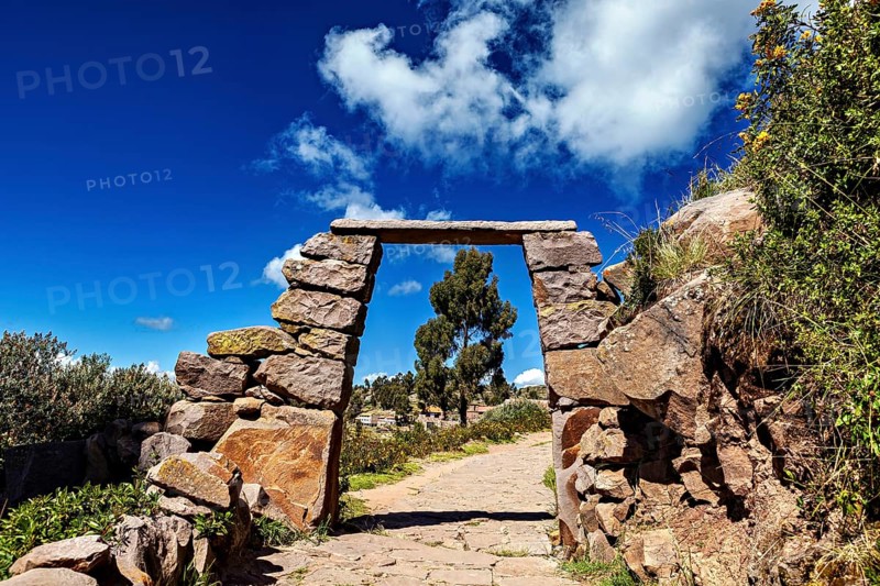 A rectangular stone arch under a cloudy sky, with a path that leads into nature, stone gates on Taquile Island in Lake Titicaca in Peru