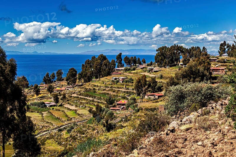 A terraced village stretches along a hill overlooking a blue lake, countryside and farmhouses on Taquile Island in Lake Titicaca in Peru
