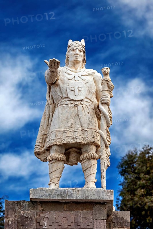 Stone statue of a warrior with a raised hand against a blue sky, Great Inca monument on Taquile Island in Lake Titicaca in Peru