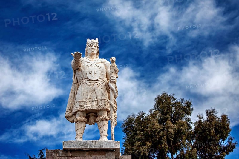 Stone statue of a warrior against a cloudy, blue sky, Great Inca monument on Taquile Island in Lake Titicaca in Peru