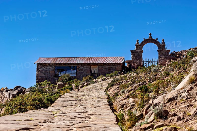 Stone house with archway along a path under a blue sky, stone gates on Taquile Island in Lake Titicaca in Peru