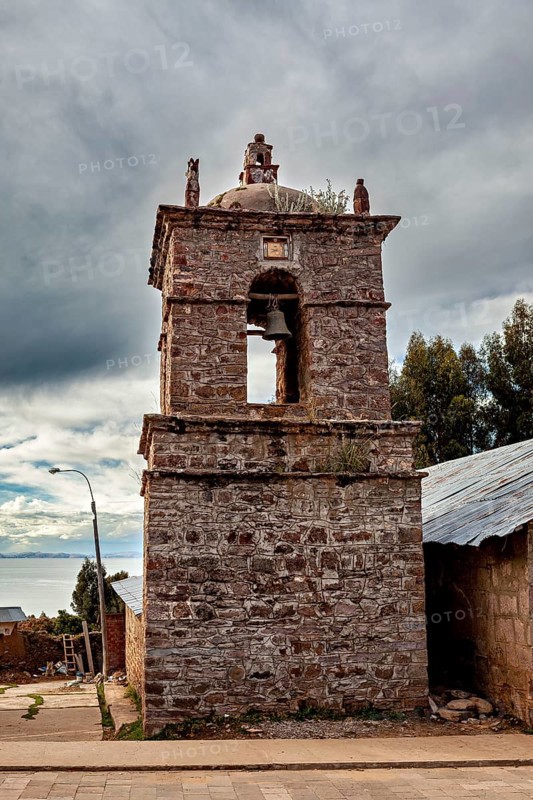 An old stone bell tower in cloudy sky surrounded by rustic landscape, The historic church on Taquile Island in Lake Titicaca in Peru