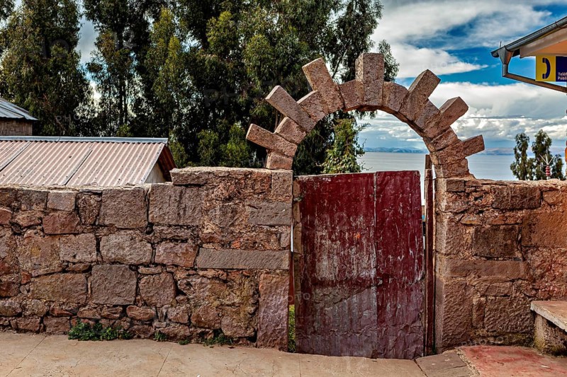 Stone wall with wooden gate and views of sky and nature, stone gates on the island of Taquile in Lake Titicaca in Peru