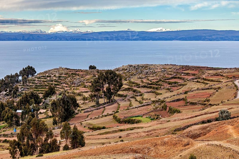 Landscape with a wide view over fields, a lake and a cloudy sky on the horizon, The countryside and farmhouses on the island of Taquile in Lake Titicaca in Peru