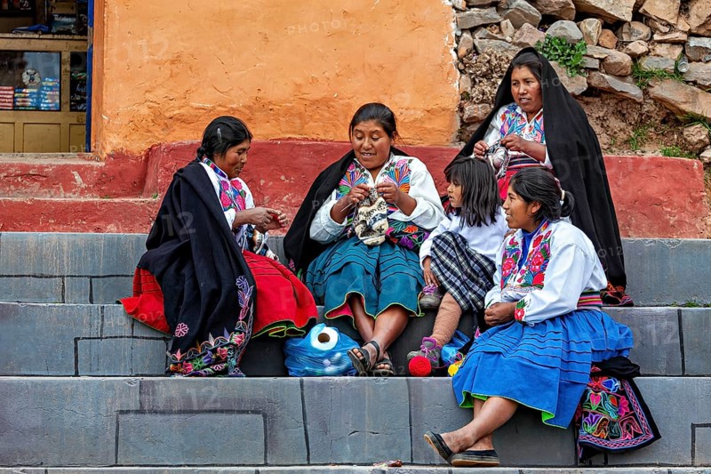 Women and children in traditional clothing sit on steps and interact with each other, the woman on Taquile Island in Lake Titicaca in Peru