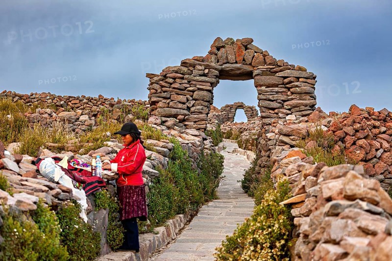 Woman next to clothes on traditional path with stone walls, stone gates on Taquile Island in Lake Titicaca in Peru