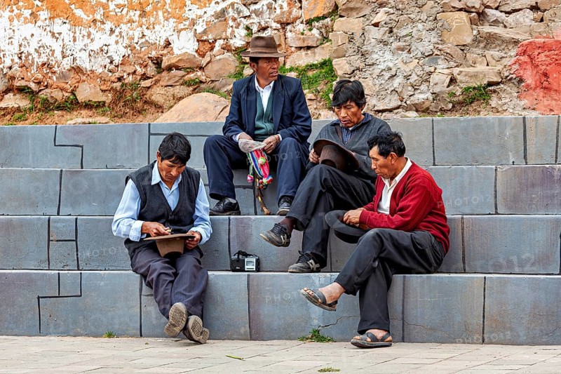 Four men in traditional clothing sit relaxed on stone steps in an urban setting, men sit together on the island of Taquile in Lake Titicaca in Peru