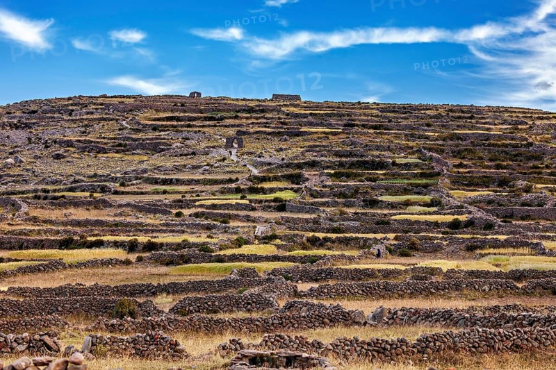 Terraced landscape on a hill under a dramatic sky with stone walls, The countryside and farmhouses on Taquile Island in Lake Titicaca in Peru