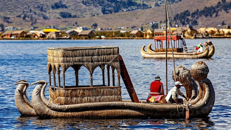 Traditional reed boat with people on a calm lake in front of a shore with reed huts, The floating reed islands of the Uros in Lake Titicaca in Peru